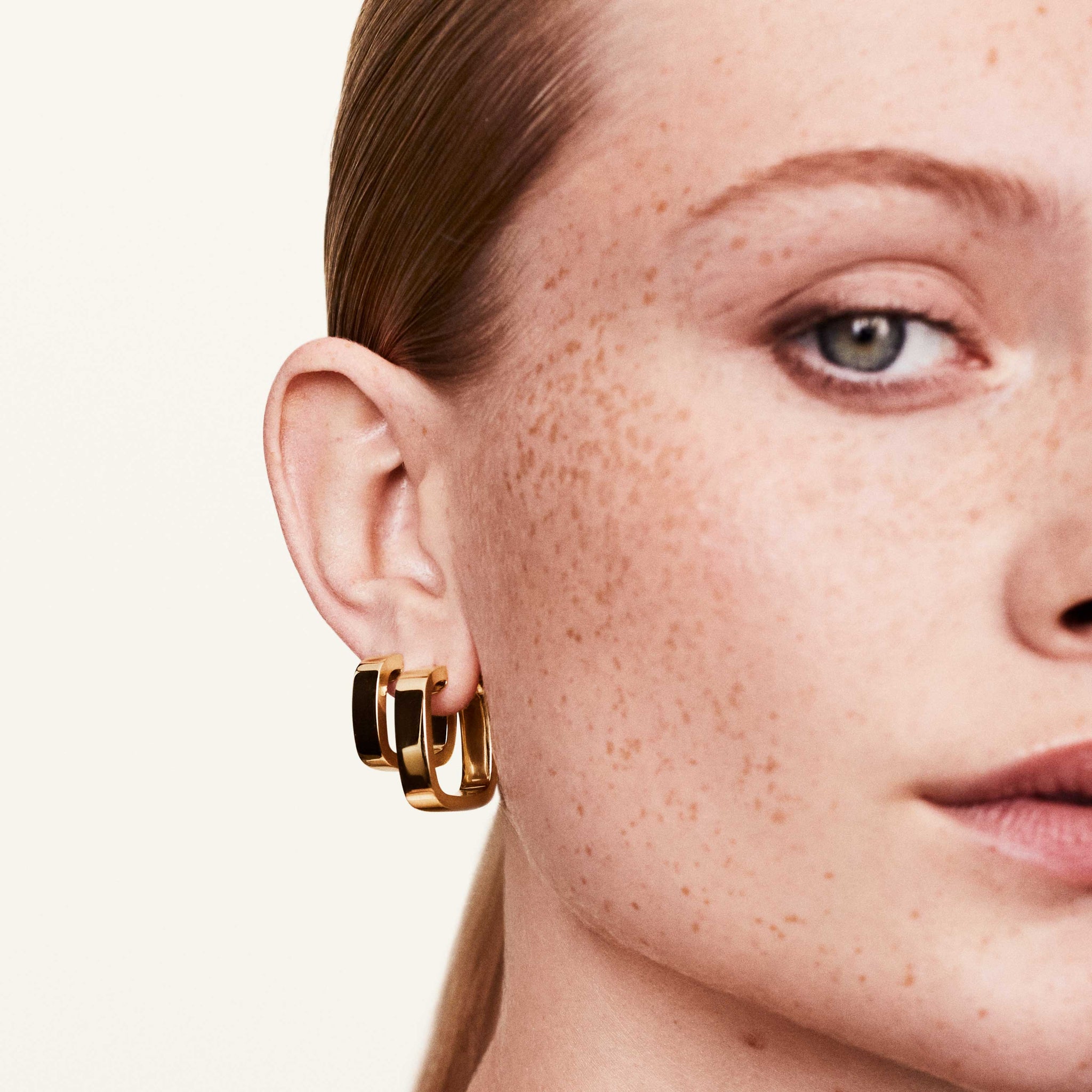 A person wearing gold square hoop earrings