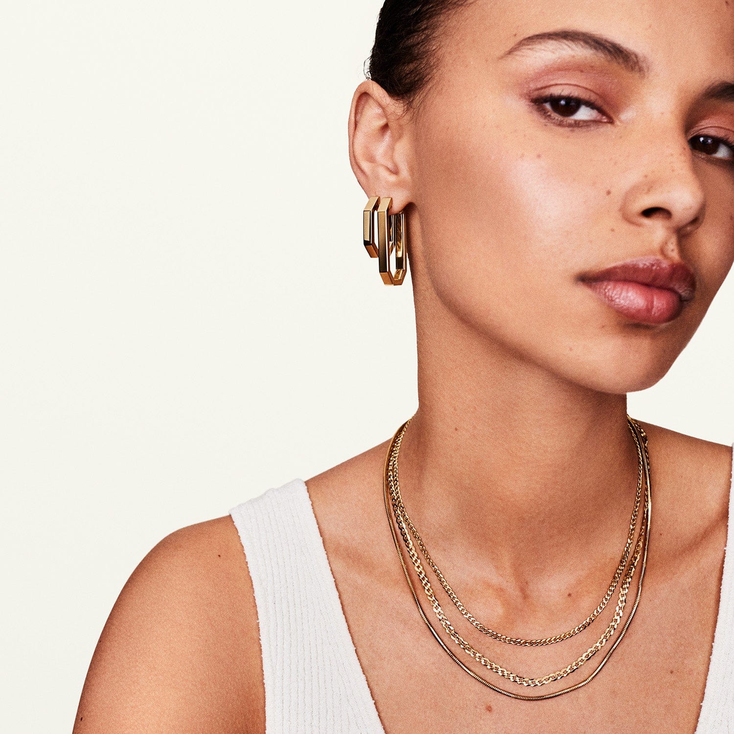 Woman wearing a 14k gold curb chain layered with other chain necklaces.