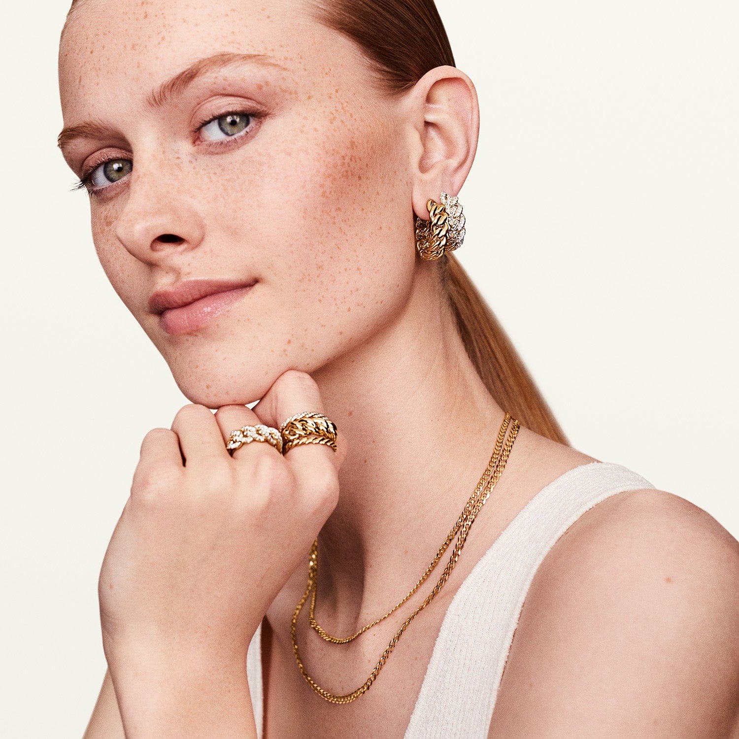 A woman posing with a 14k yellow gold pave infinity ring, complemented by matching earrings and necklaces.