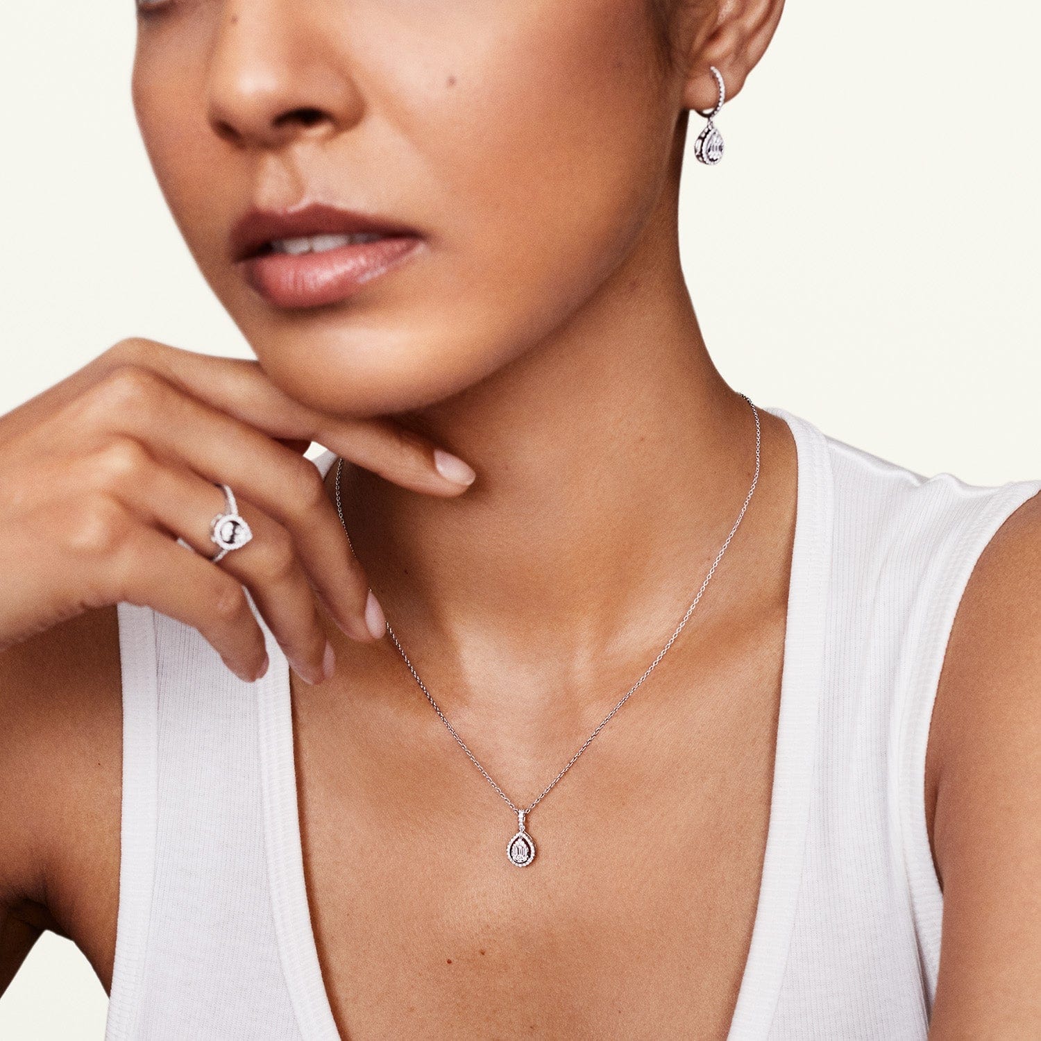 Model wearing drop halo earrings with matching ring and pendant