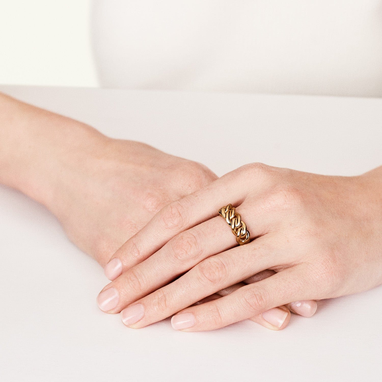 A hand wearing a gold link ring with a chain style pattern.
