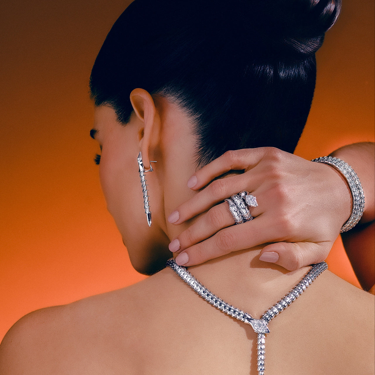 Woman wearing a diamond necklace, earrings, and ring against an orange background
